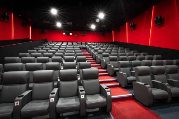 wide angle view of a modern empty cinema movie theatre with rows of dark seating and spot lights shining down with red walls